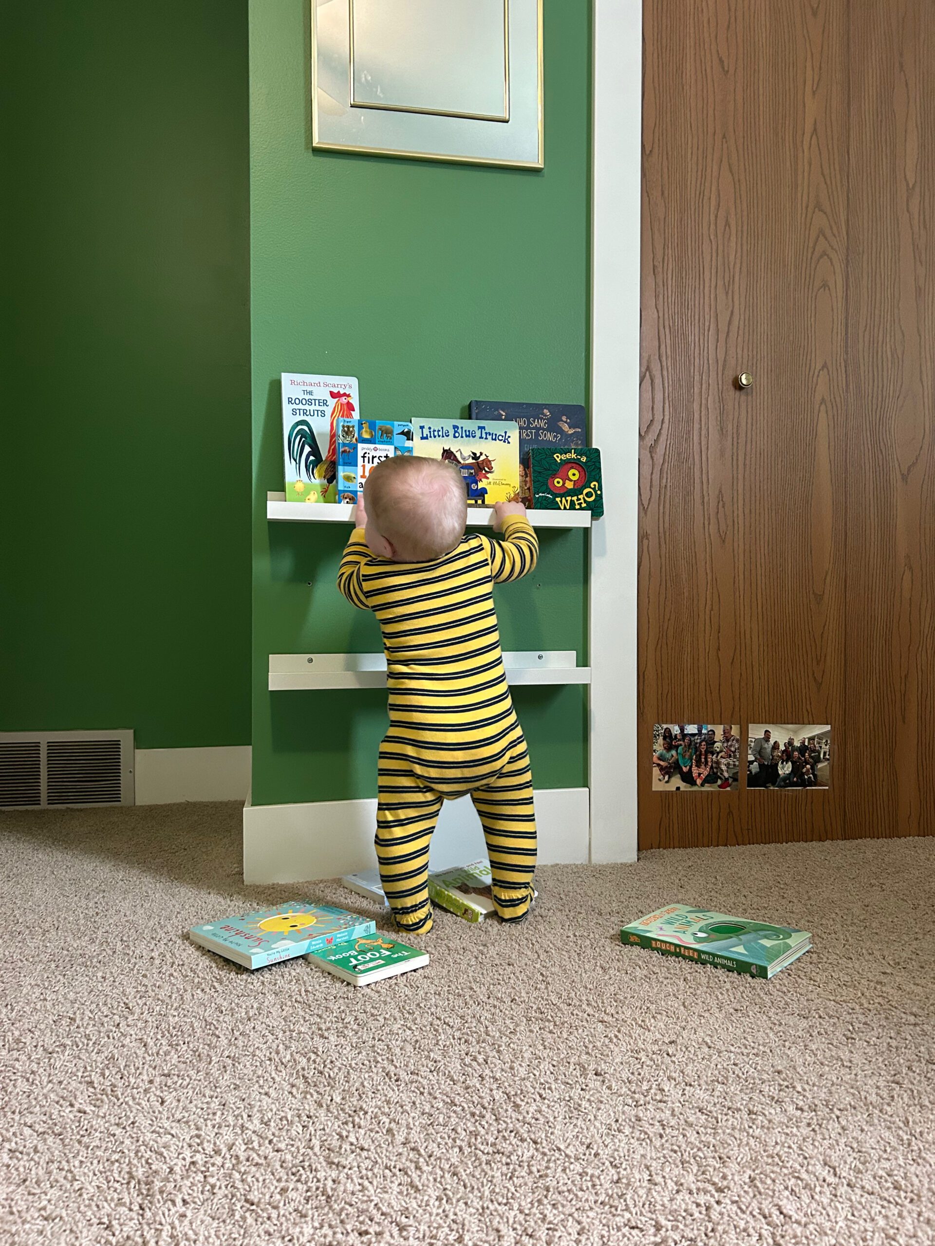 Baby boy holding on to a book shelf to help him balance and learn to walk.