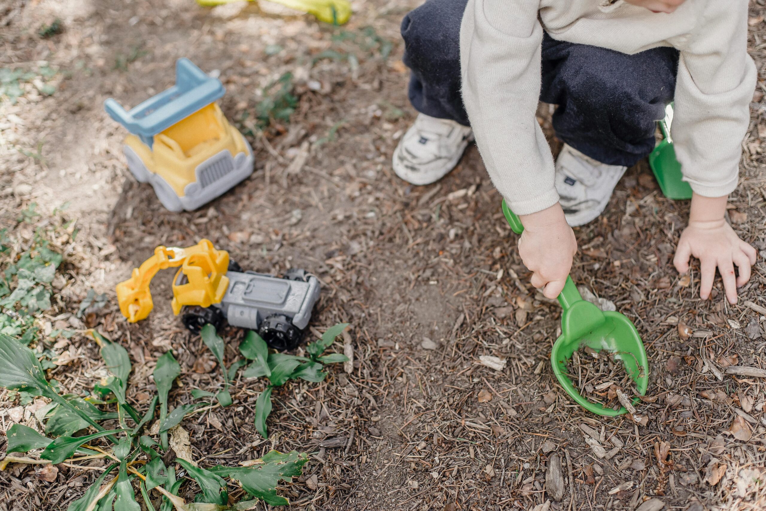 Summer essentials for babies and toddlers. Picture of a toddler digging in the dirt with some toy trucks